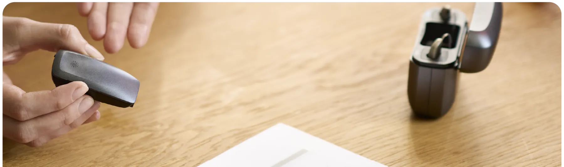 Atención en mostrador con un audífono, su cargador y documentación sobre la mesa